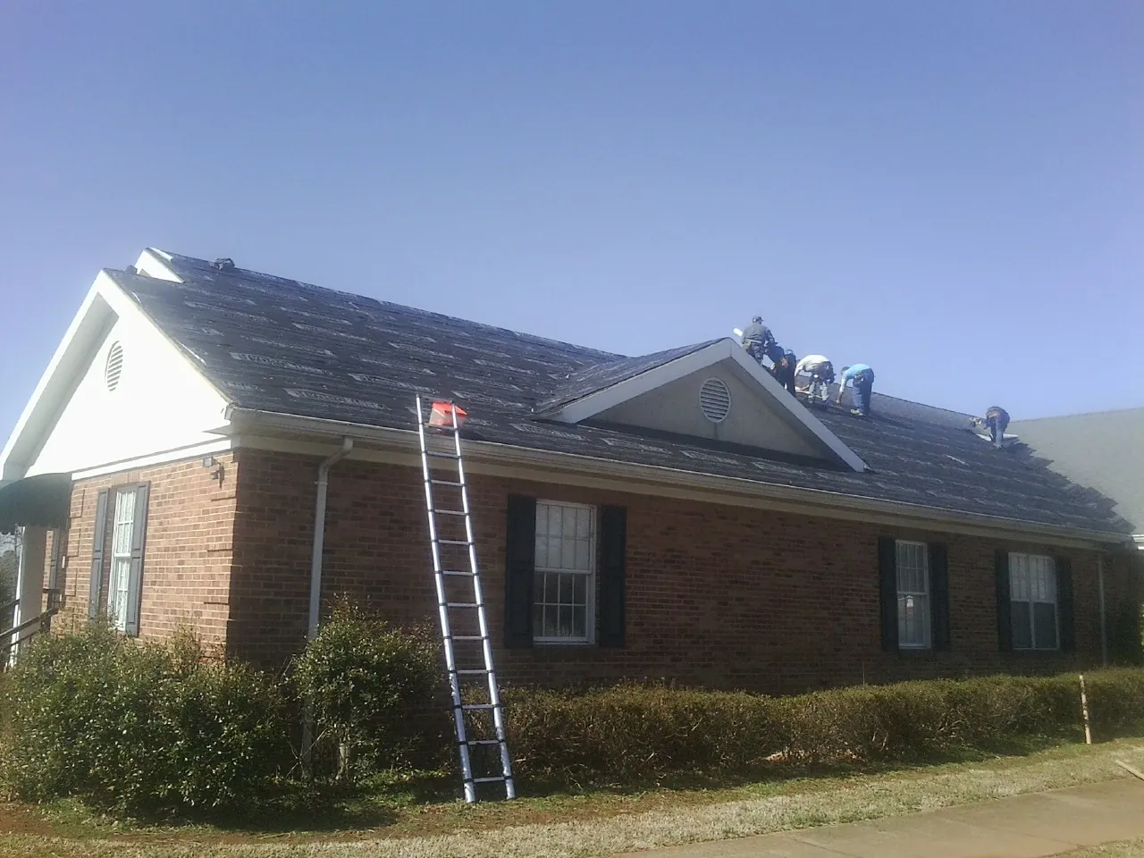 Crew tearing shingles off a brick ranch roof with a ladder set — Metal Roof Repair work by our crew in Piscataway