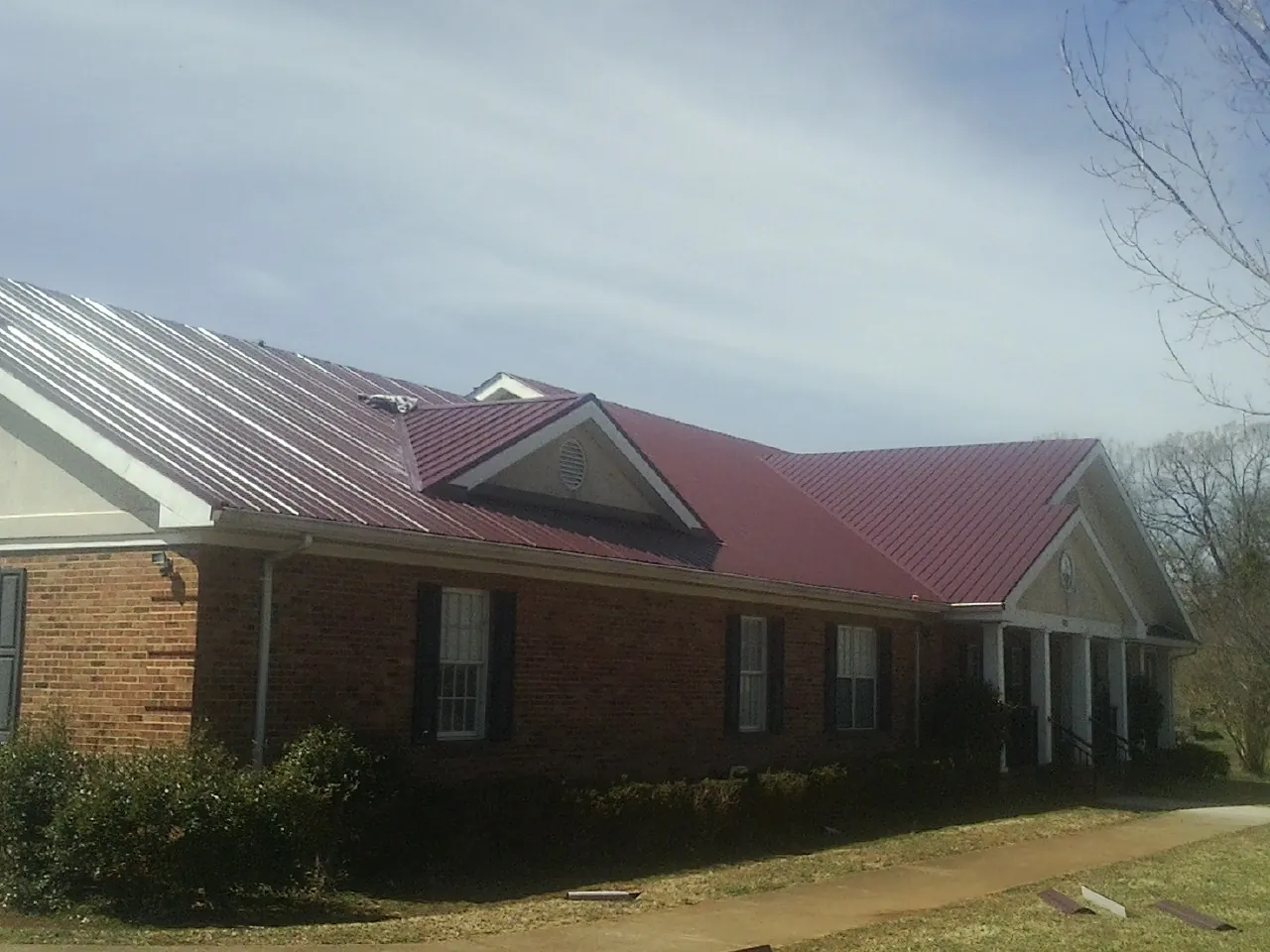 Red metal roof with gabled entries on a long brick building, from a Hail Damage Roof Repair job in Piscataway