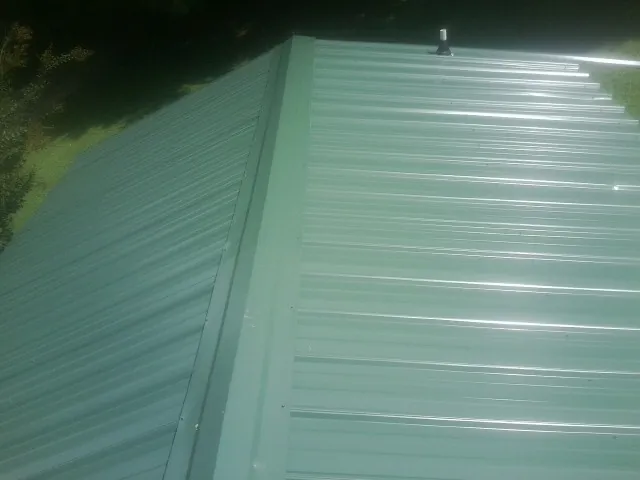 New green metal panels meeting at the ridge of a roof — Flat Roof Repair work by our crew in Piscataway