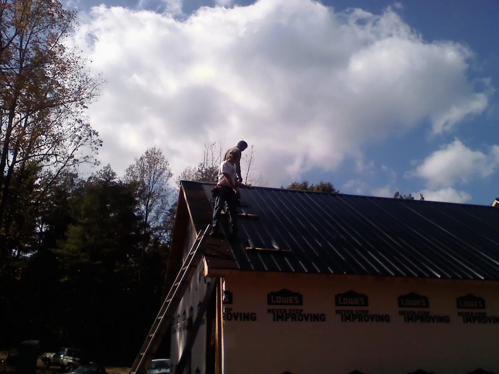 Roofer fastening dark metal panels high against a cloudy sky, from a Roof Inspection job in Piscataway