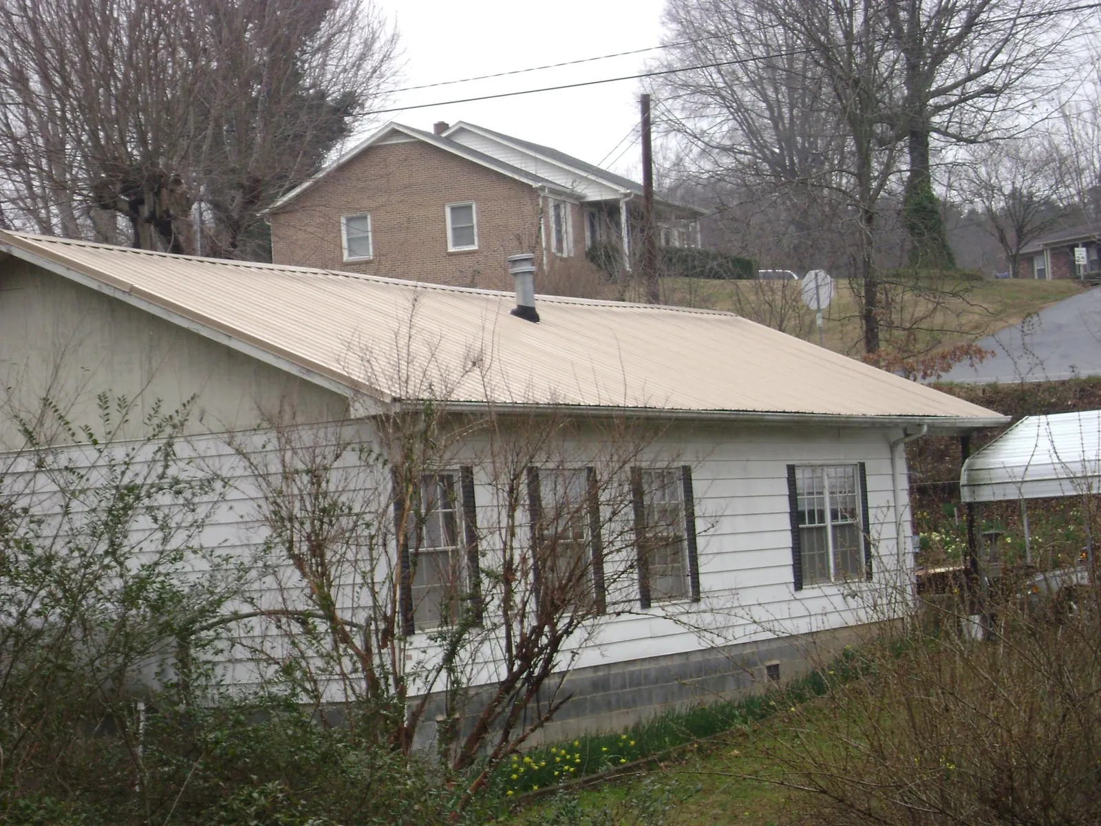 Tan metal roof on a white sided house set into a hillside — Commercial Roofing by Roofing Brothers in Piscataway